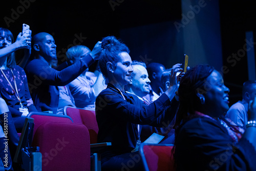 Audience members with smart phones videoing speaker on stage at conference