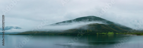 Misty Lake As Fog Rolls Against A Green Mountain Background