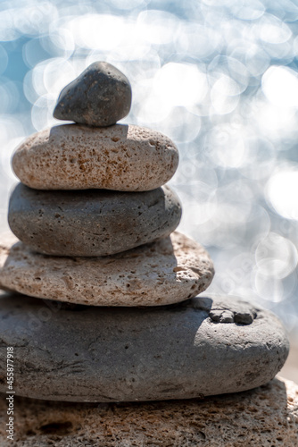 A tower of stones. Balanced pyramid of pebbles on the beach on a sunny day. Blue sea in the background. Selective focus  bokeh. Zen stones on the sea beach  meditation  spa  harmony  tranquility