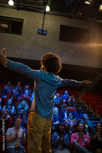 Audience watching male speaker with arms outstretched on stage © KOTO