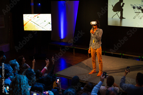 Audience watching male speaker with virtual reality simulator glasses on stage