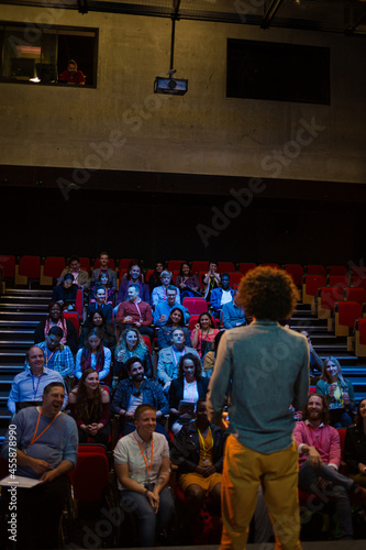 Audience watching male speaker with arms outstretched on stage