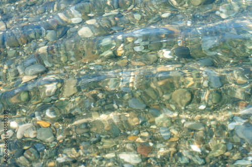 Background of wet pebbles on the bottom of the sea, which is washed by a sea wave