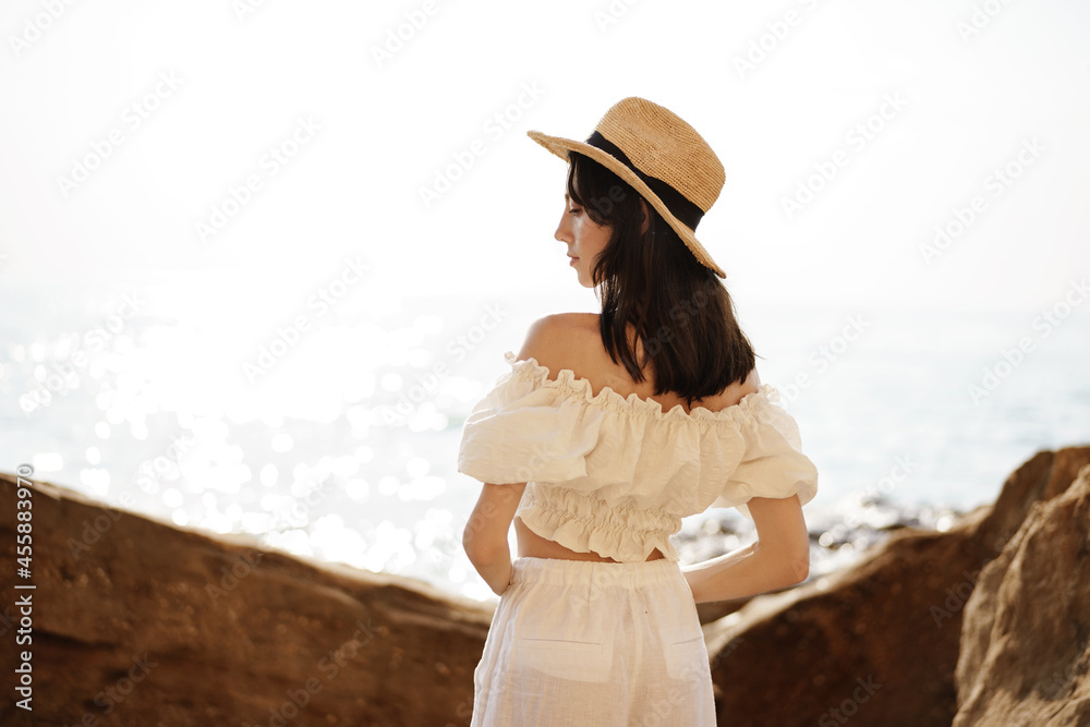 Young joyful brunette woman posing against sea and rocks