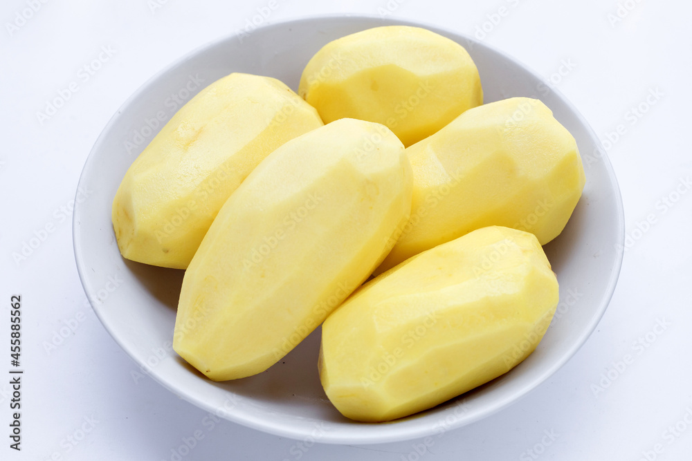 Raw peeled potatoes in white bowl on white background