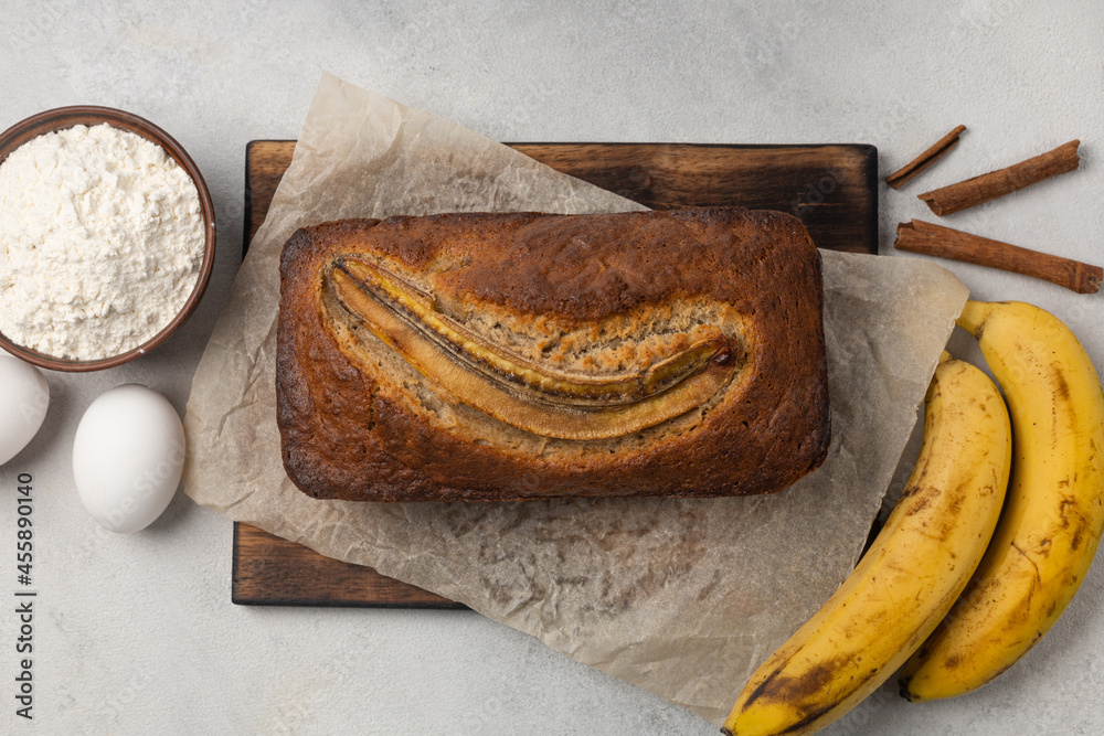 Ready fresh banana bread in a rectangular baking dish with ingredients on a light background