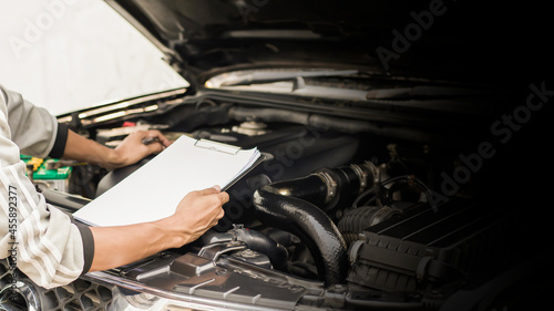 Automobile mechanic repairman checking a car engine with inspecting writing to the clipboard the checklist for repair machine, car service and maintenance.
