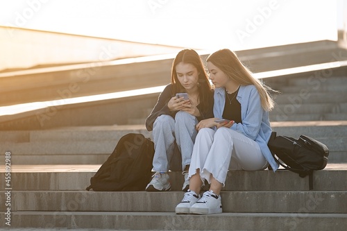Bilde på lerret Two teenage students girls at the building of university using smartphone, back