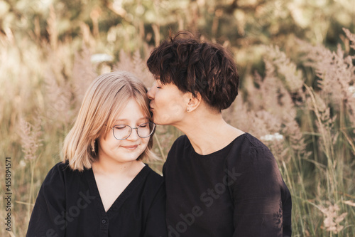 A mother kisses her teenage daughter in nature in the summer