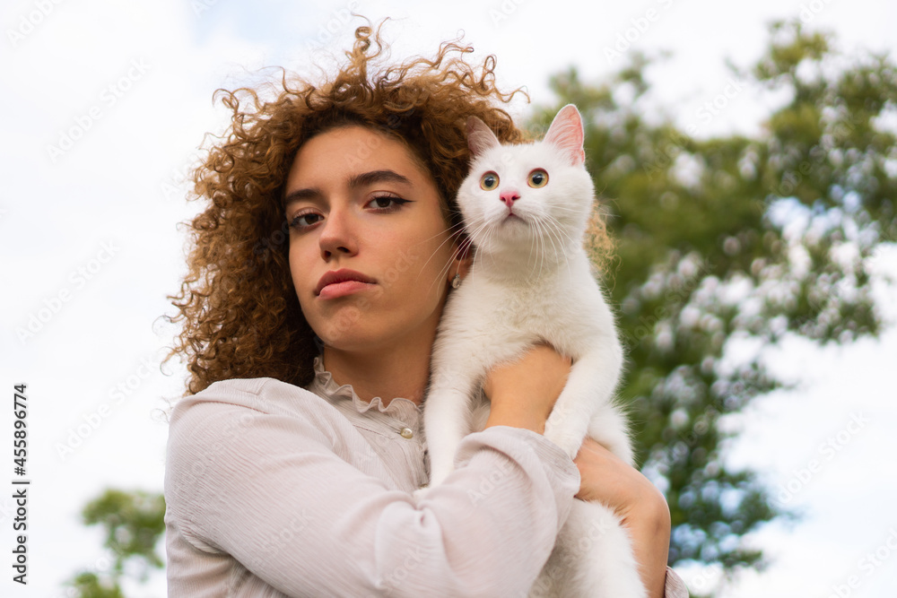 A beautiful teenage girl with curly hair holds a white cat close to her face. She is enjoying time with her pet. A beautiful teenage girl with curly hair holds a white cat close to her face. She is enjoying time with her pet.