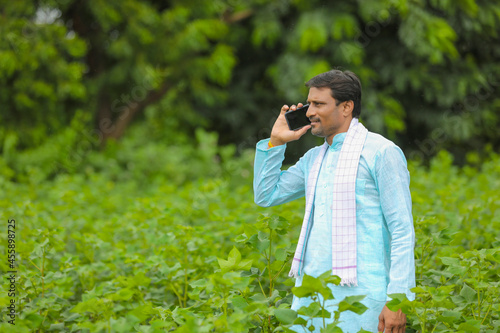 Indian farmer talking on smartphone at green agriculture field