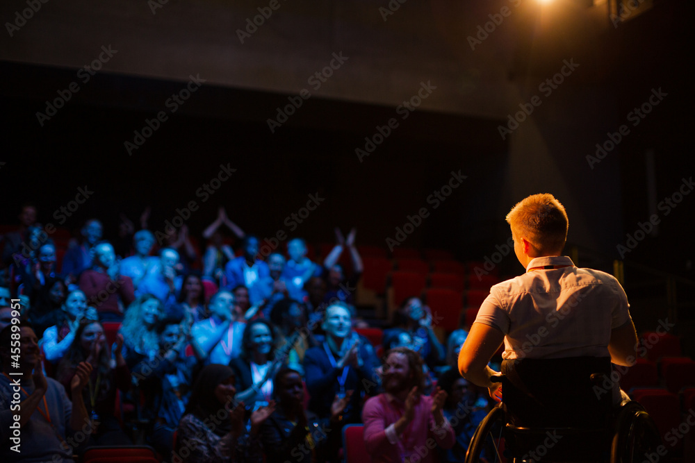 Female speaker in wheelchair on stage waving to audience