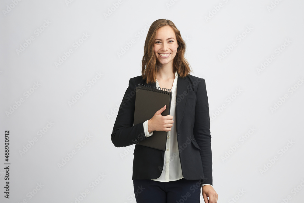 Beautiful young business woman with folder in her hand smiling and looking happy in camera while standing isolated Beautiful young business woman with folder in her hand smiling and looking happy in camera while standing isolated