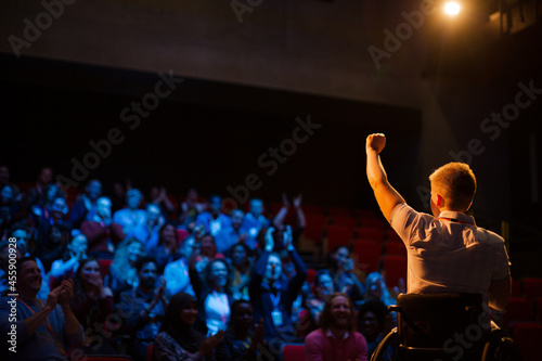 Female speaker in wheelchair on stage waving to audience © KOTO