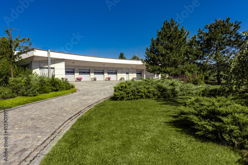 Modern garage for several cars with paved driveway surrounded by green parkland © nazarovsergey