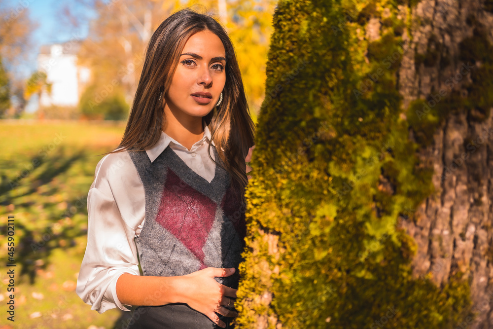 A young Caucasian brunette college girl, in a park next to a tree one autumn afternoon A young Caucasian brunette college girl, in a park next to a tree one autumn afternoon