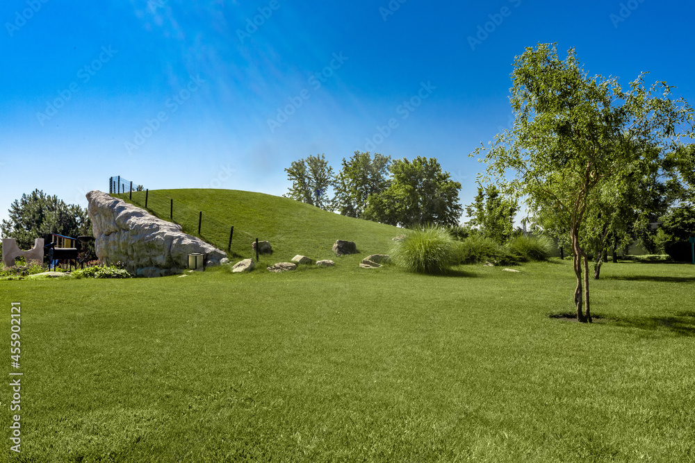 Park area with trimmed lawn grass on hillside of rock structure and children playground