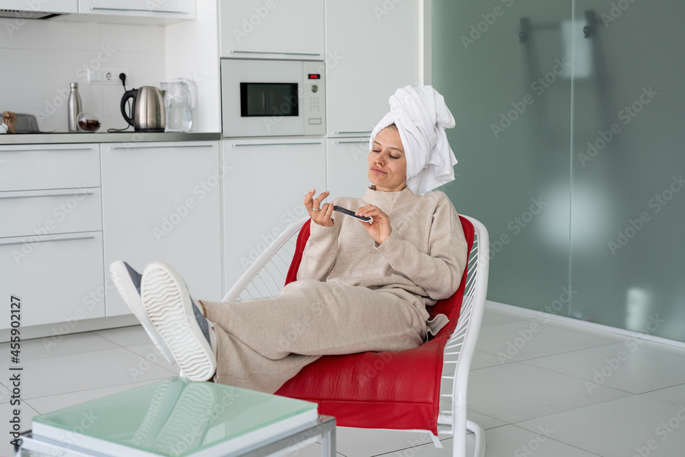 Funny young housewife with bathtowel on her head sitting in the chair doing manicure Funny young housewife with bathtowel on her head sitting in the chair doing manicure