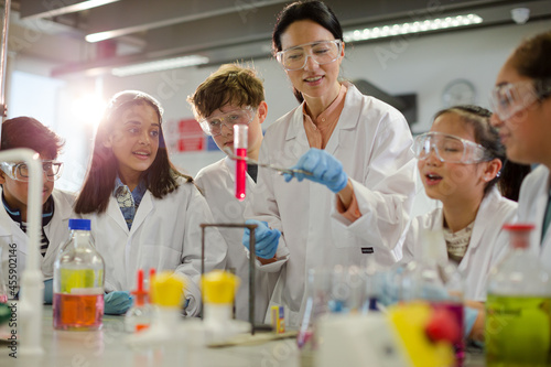 Female teacher and students conducting scientific experiment, watching liquid in test tube in laboratory classroom