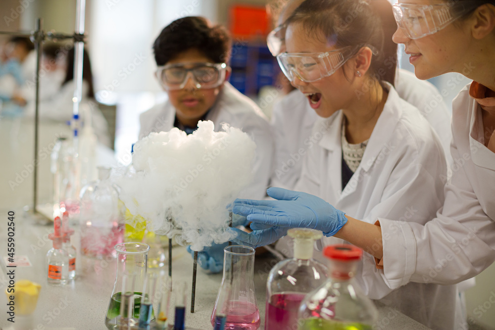 Female teacher and students watching scientific experiment chemical reaction in laboratory classroom Female teacher and students watching scientific experiment chemical reaction in laboratory classroom