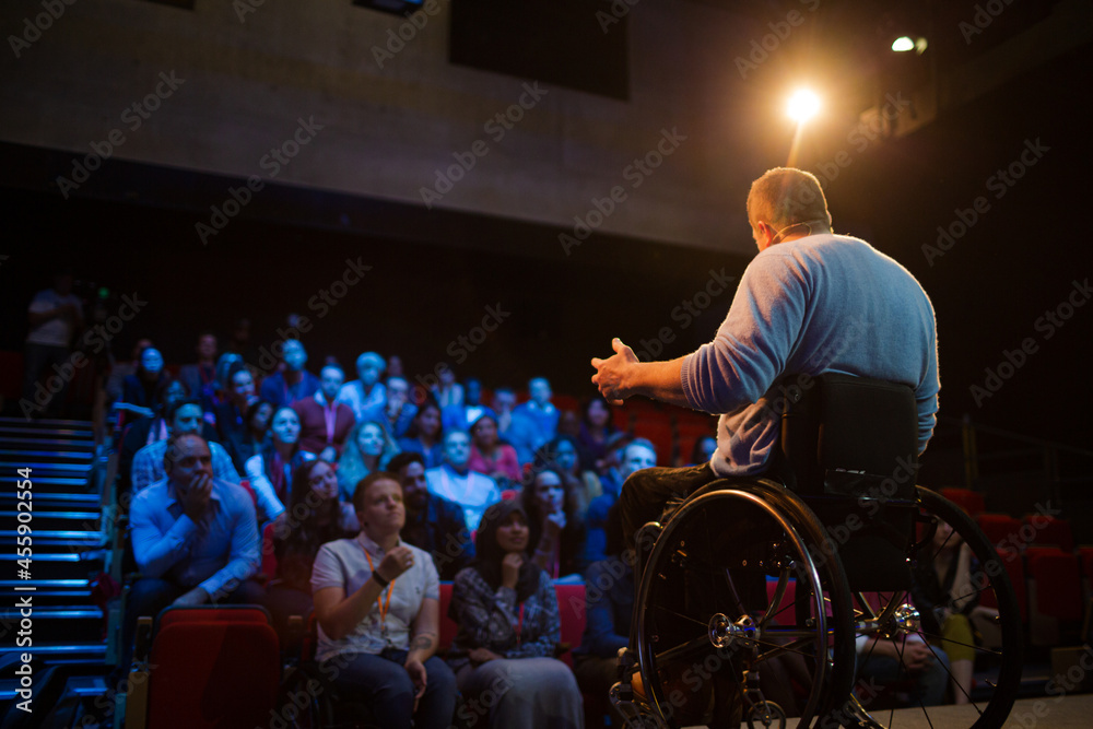 Audience watching male speaker in wheelchair talking on stage Audience watching male speaker in wheelchair talking on stage