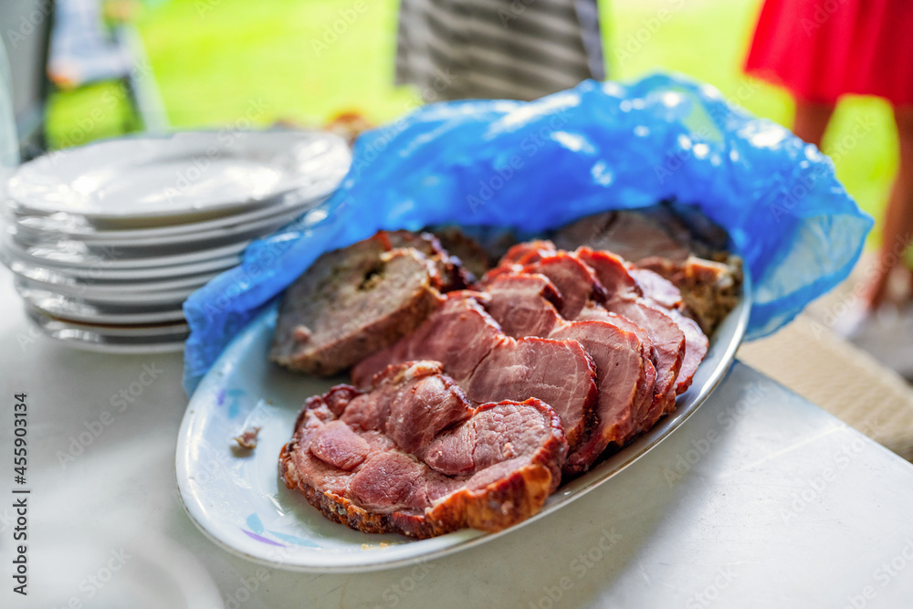 Plate with smoked meat, plastic bag, pile of empty plate, people in garden.
