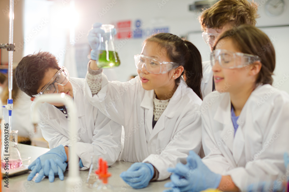 Obraz premium Curious students conducting scientific experiment, examining liquid in beaker in laboratory classroom