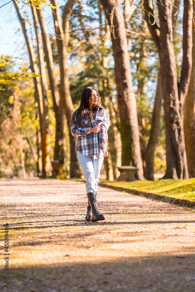 Fototapeta premium Autumn lifestyle, a young Caucasian brunette girl in a plaid wool sweater and ripped jeans in a park