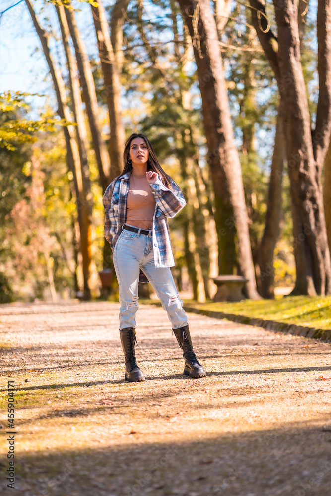 Lifestyle, a young Caucasian brunette girl in a plaid wool sweater and ripped jeans in a park in autumn