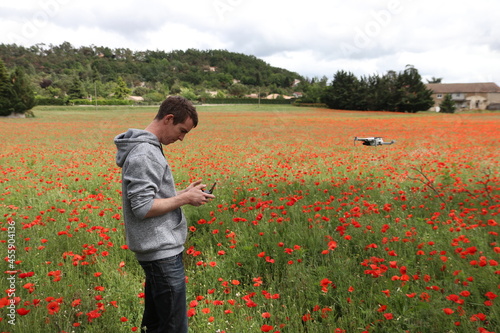 A man drone pilot flies a mini drone in a field of poppies. Country summer environment. Image with selective focus.