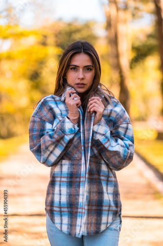 Lifestyle, young Caucasian brunette with a plaid wool sweater and ripped jeans walking in a park in autumn