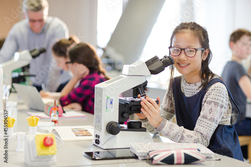 Portrait smiling, confident girl student using microscope, conducting scientific experiment in laboratory classroom