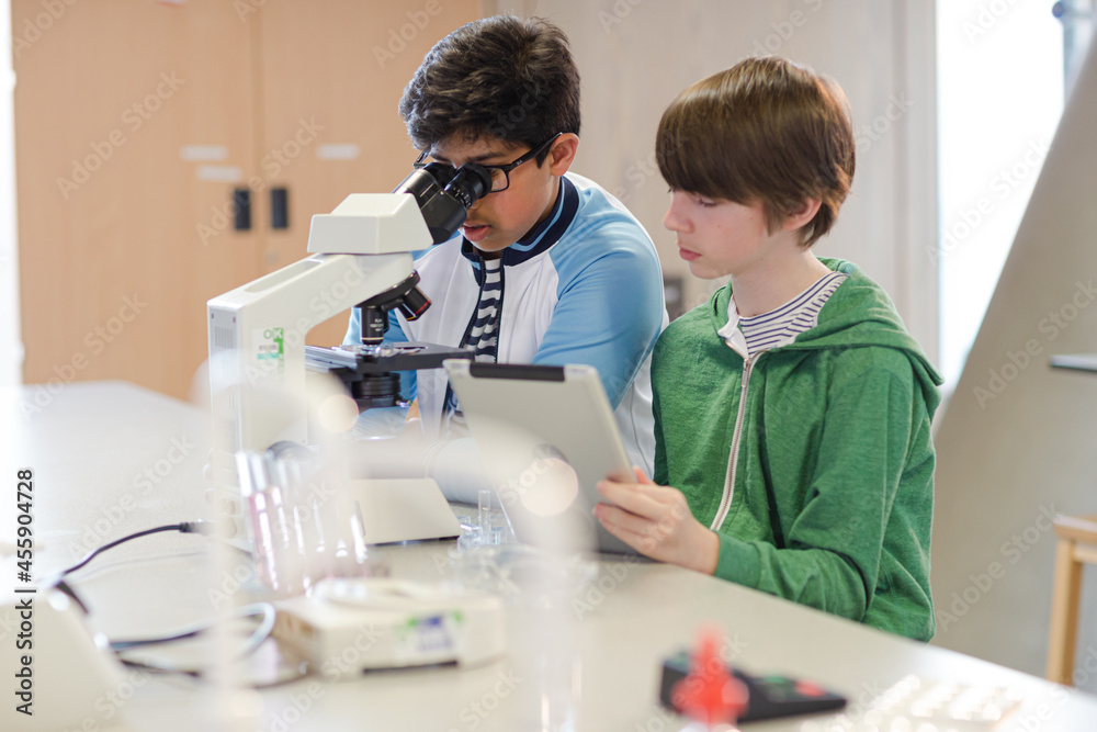 Focused boy students using digital tablet at microscope in laboratory classroom Focused boy students using digital tablet at microscope in laboratory classroom