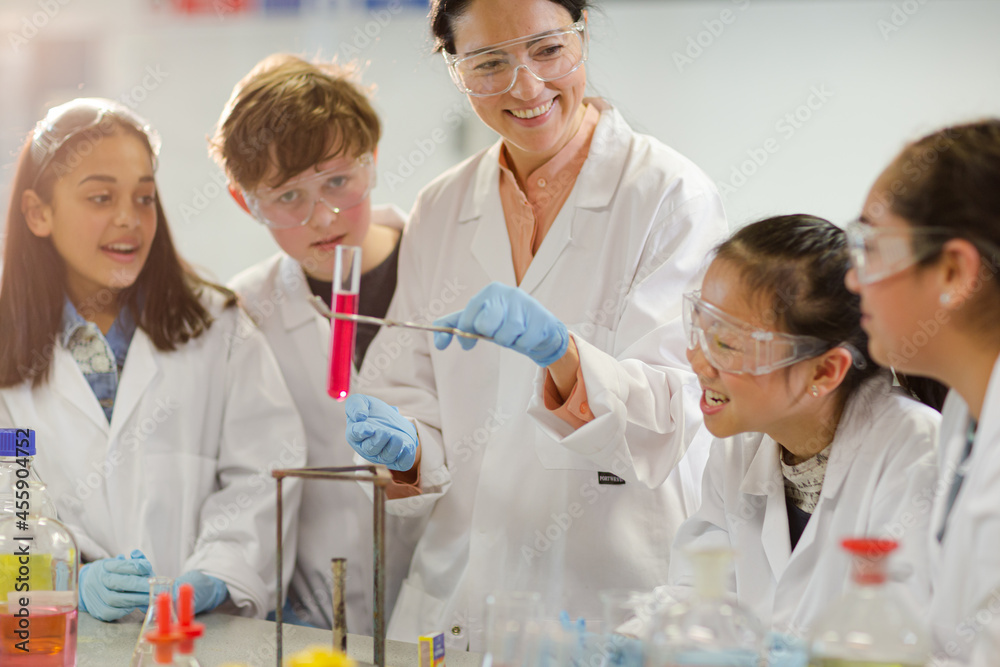 Female teacher and students conducting scientific experiment, watching liquid in test tube in laboratory classroom Female teacher and students conducting scientific experiment, watching liquid in test tube in laboratory classroom