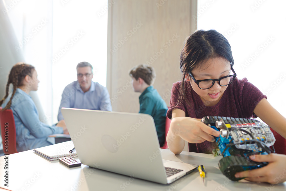 Girl student using laptop while assembling robot Girl student using laptop while assembling robot