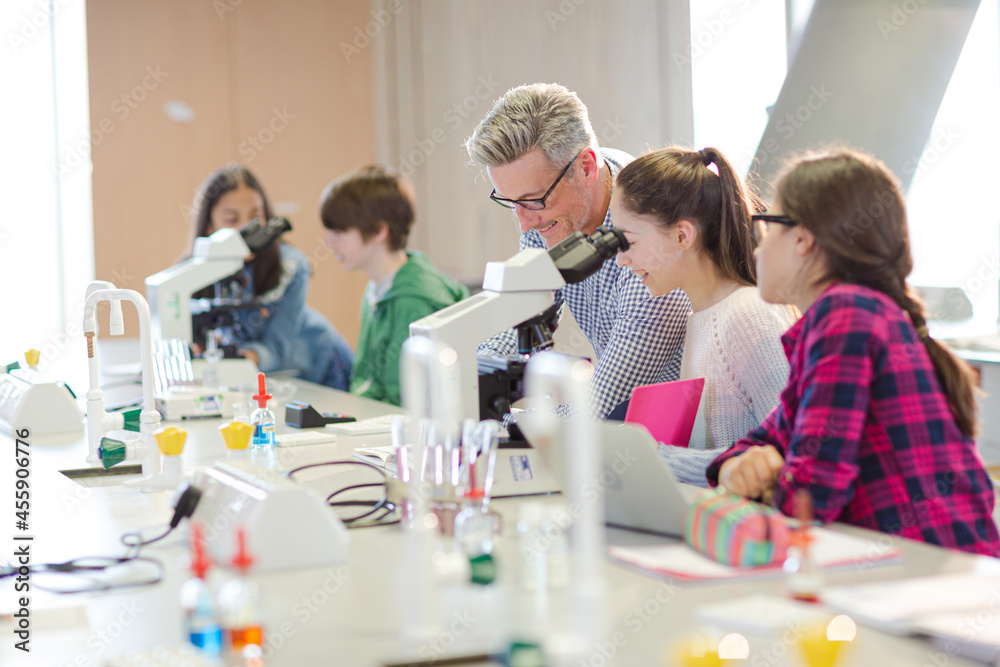 Male teacher helping girl students at microscope in laboratory classroom