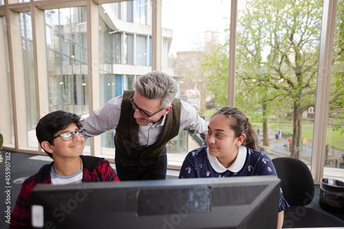 Male teacher and students using computer in library