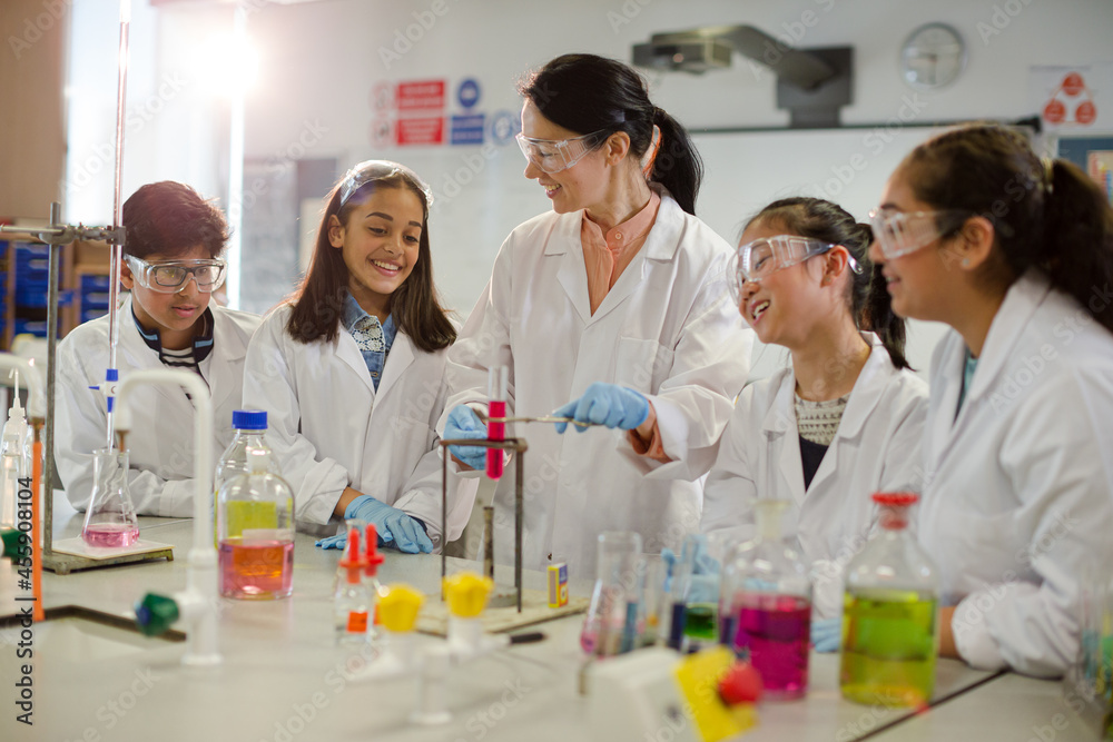 Female teacher and students conducting scientific experiment, watching liquid in test tube in laboratory classroom