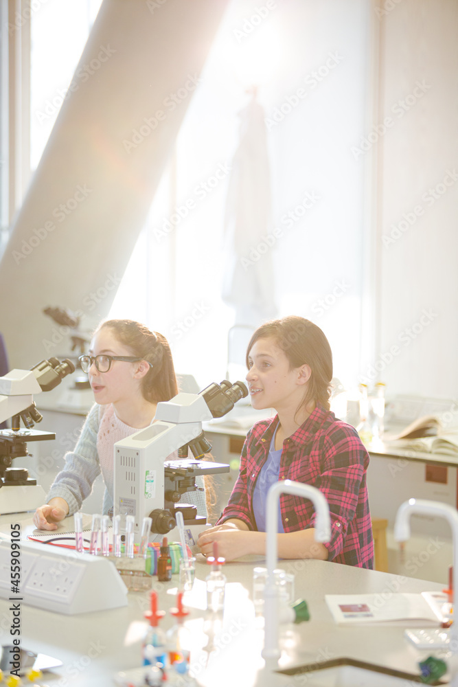 Eager girl students behind microscopes in laboratory classroom