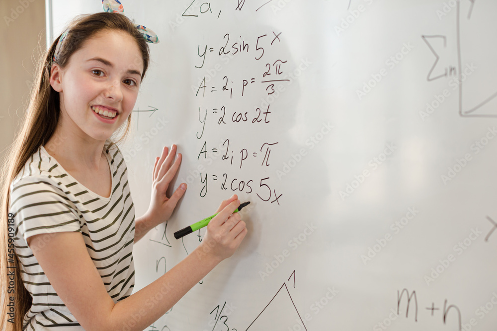 Fototapeta premium Girl student writing at whiteboard in classroom