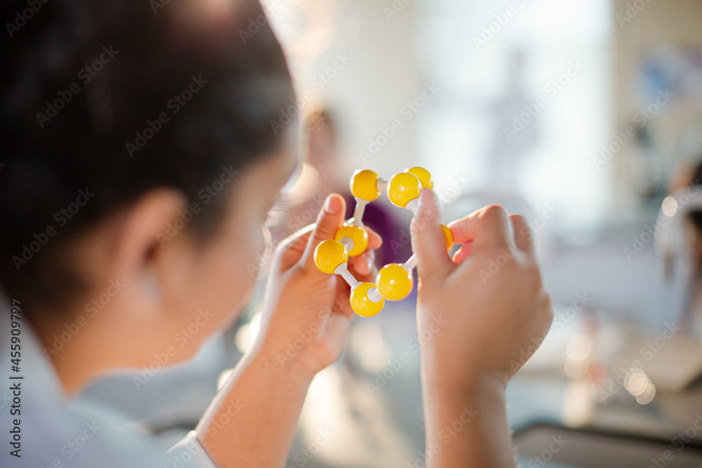 Curious girl student holding molecule model in classroom