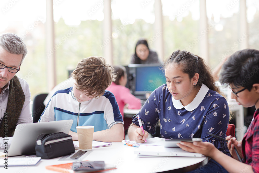 Male teacher and students using laptop at table