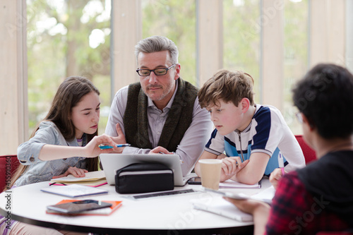 Male teacher and students using laptop at table