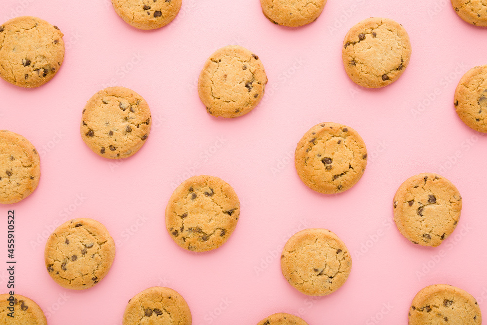 Dry cookies with chocolate pieces on light pink table background. Pastel color. Closeup. Sweet snacks. Biscuit pattern. Top down view. Dry cookies with chocolate pieces on light pink table background. Pastel color. Closeup. Sweet snacks. Biscuit pattern. Top down view.