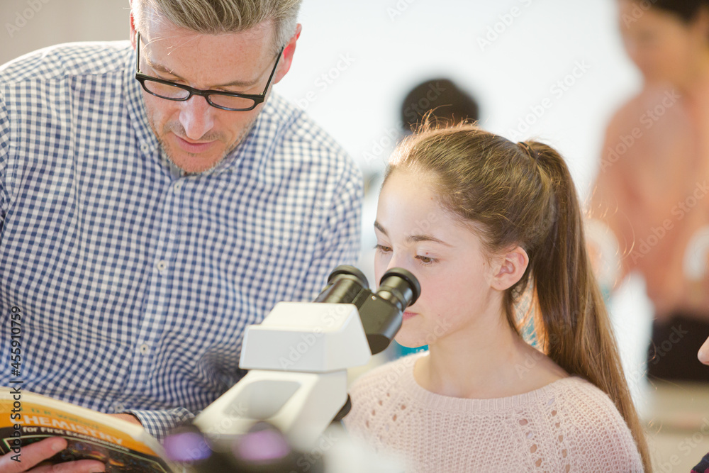 Obraz premium Male teacher helping girl student at microscope in laboratory classroom