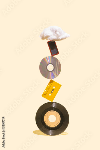 EP vinyl records, cd, cassette tape, CD, MP3 player and cotton cloud shaped prop on the top of each other. History of music mediums concept made on beige background.