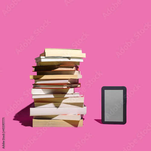 Past and present reading books inspired concept. E book reader stand alone beside the many books against purple background.
