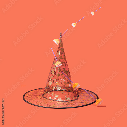 Halloween arrangement witch back hat with golden glitter prints with colorful broomsticks levitating around it. Minimal terracotta background. photo