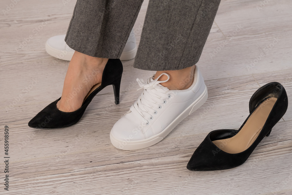 Close-up business woman takes off her shoes puts on white leather sneakers. Close-up business woman takes off her shoes puts on white leather sneakers.