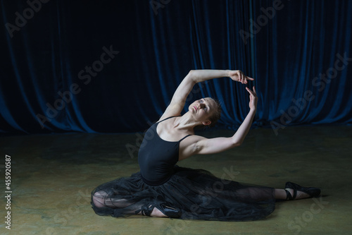 A ballerina in a black ballet costume rehearses on stage.